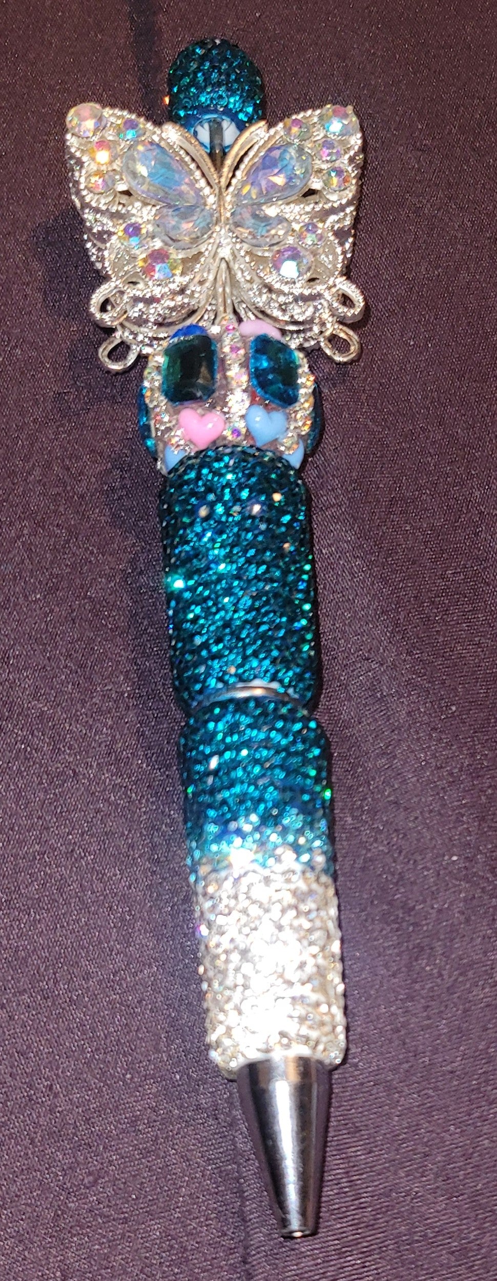 Decorative pen with butterfly design and blue glittery body on a purple background